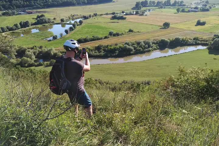 Cyclist in helmet photographing scenic Transylvania river valley and farmland from hilltop viewpoint