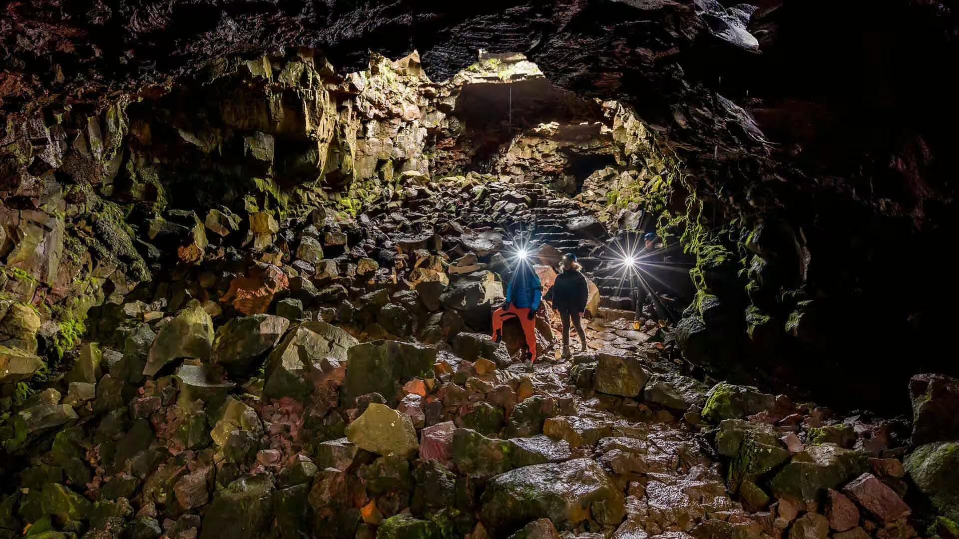 Explorers with headlamps walking through a rocky lava tunnel cave in Iceland