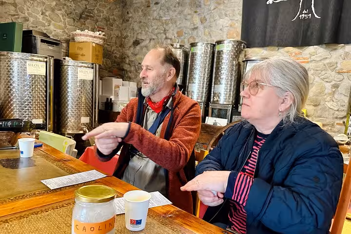 Visitors enjoy a guided olive oil tasting session in a rustic stone-walled room, surrounded by stainless steel tanks.