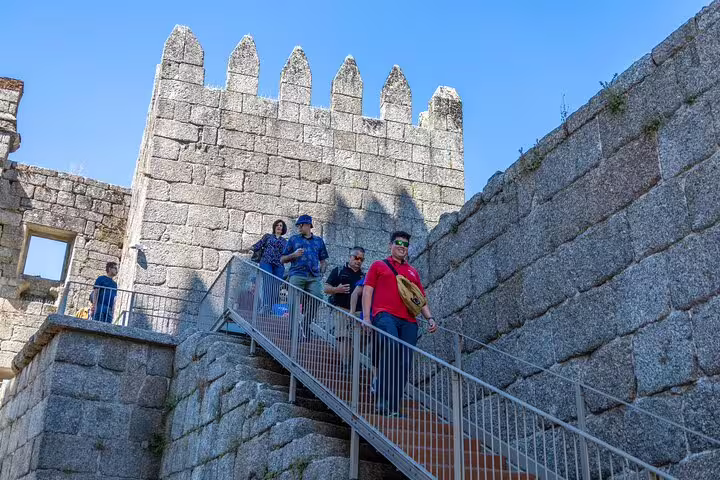 Tourists explore historic Guimarães Castle on a sunny day during a small group tour with hotel pick-up.