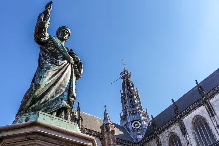 Statue and Grote Kerk Haarlem with clock tower under blue sky, highlight of a 2-hour private walking tour