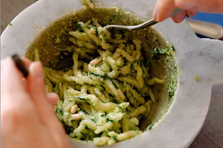 Close-up of handmade pasta being mixed with fresh pesto in a cooking class between Portofino and Cinque Terre.