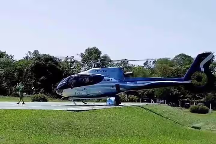 Blue and white helicopter parked on a grassy helipad surrounded by lush greenery in Foz de Iguaçu.