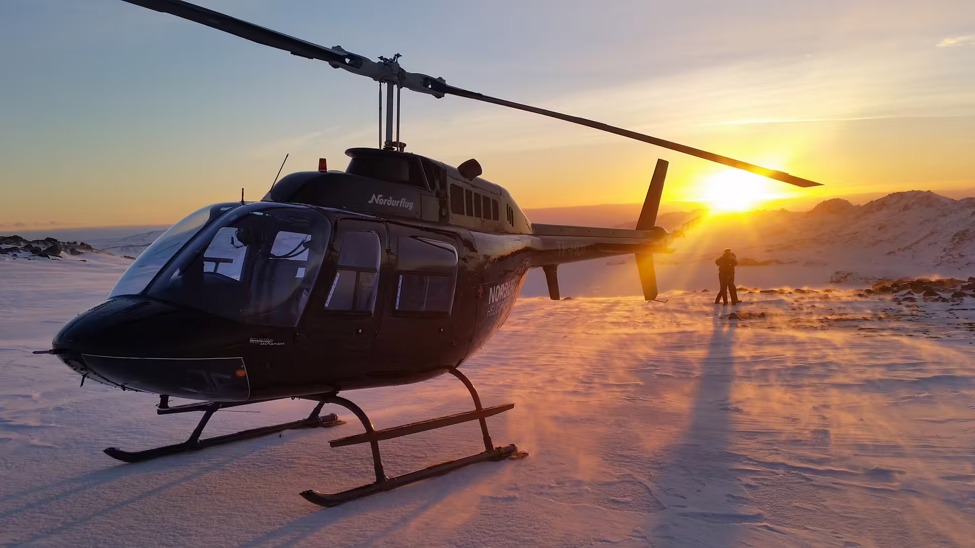Helicopter parked on snowy terrain during a vibrant sunset, offering an adventurous ATV and helicopter tour experience.