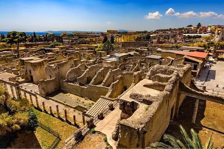 Aerial view of Herculaneum ruins showcasing ancient architecture against a backdrop of modern buildings and the sea.