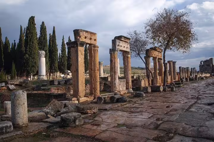 Ancient ruins of Hierapolis with stone columns and trees, a key attraction on the Pamukkale tour from Izmir.