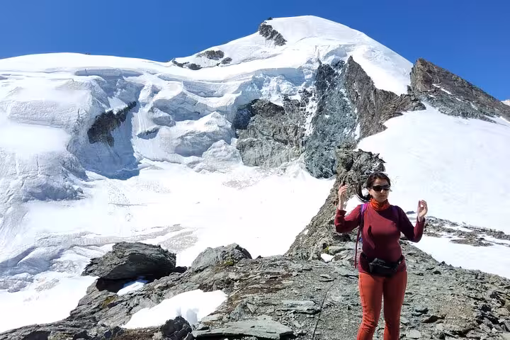 Hiker on rocky ridge below snowy Swiss glacier, part of 4-day Swiss Alps trekking tour with mountain views