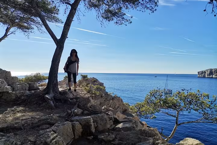 Hiker on rocky viewpoint above the Calanques near Marseille, overlooking blue sea and sailboats on a guided trek