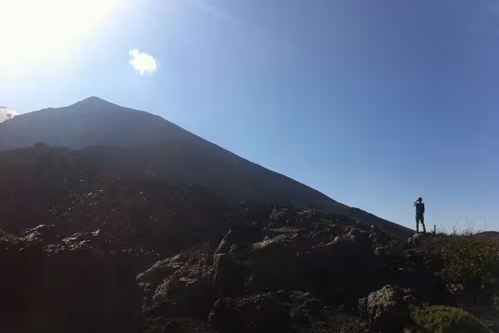 Silhouette of a hiker against Mount Etna's slopes under a clear blue sky, capturing the adventure of volcano exploration.