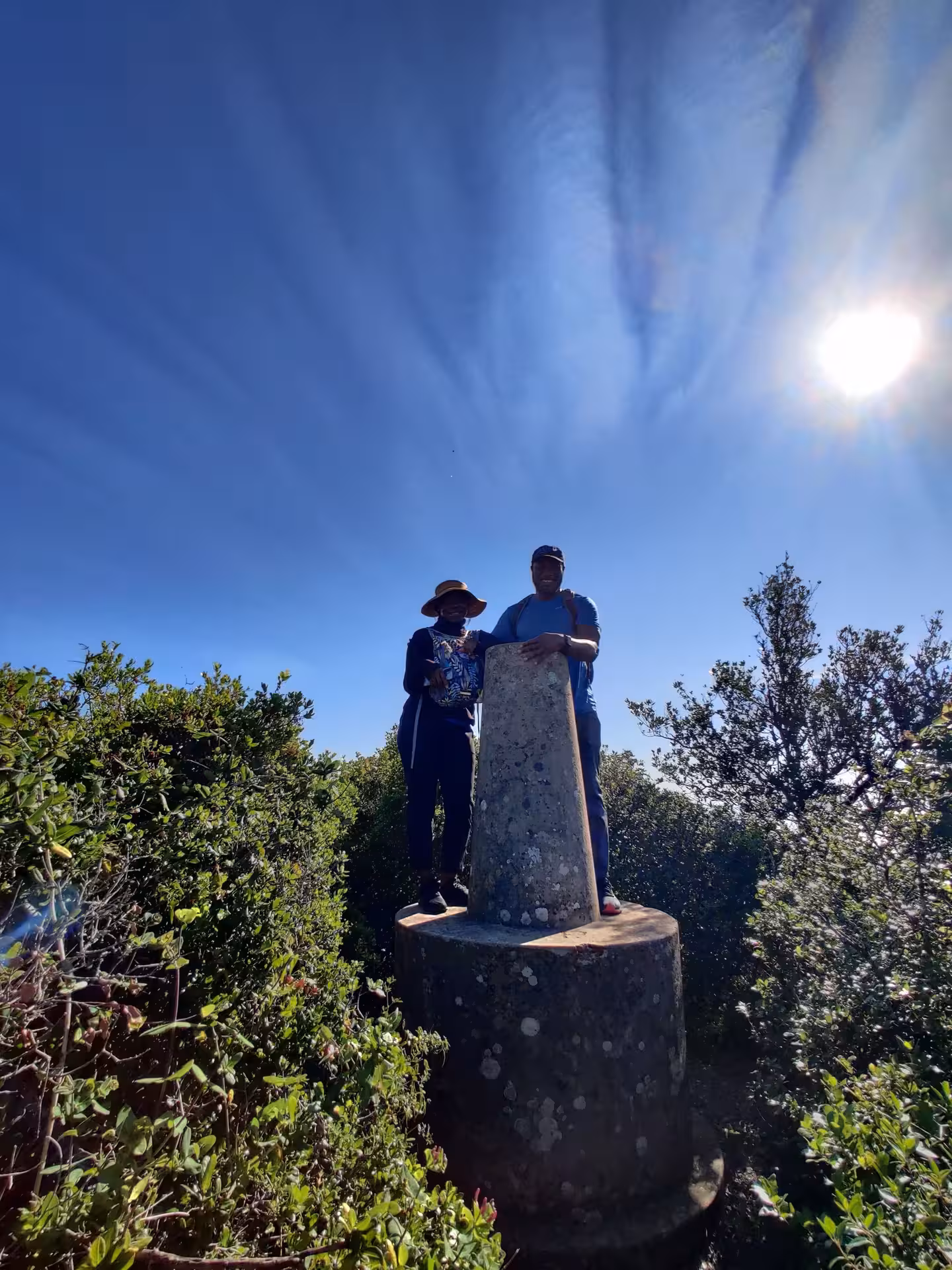 Two hikers at summit marker in Sardinia on guided trek to Capo Caccia, continental Europe’s highest sea cliff