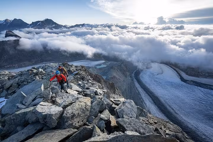 Hikers on rocky ridge above glacier and clouds, adventure highlight on Zurich Airport to Zermatt Swiss Alps tour