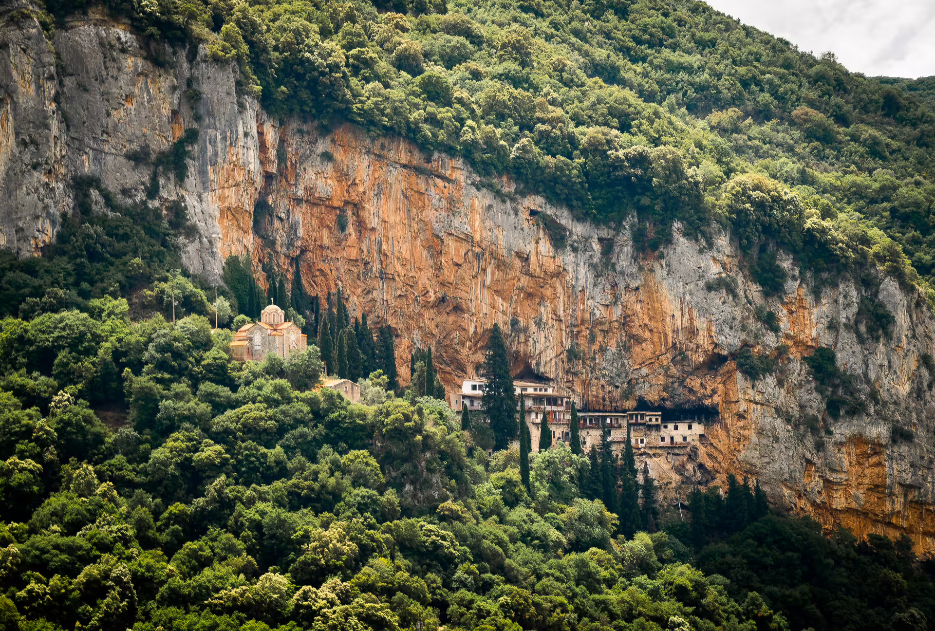 Hiking Lousios Gorge view of cliffside Prodromos Monastery above lush Arcadia forest, Peloponnese