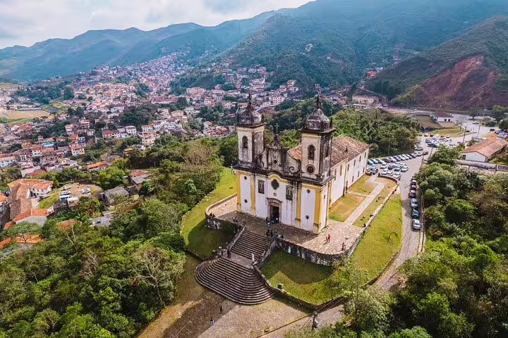 Aerial view of a historic church amidst lush greenery in Minas Gerais, part of the Gold Route tour.