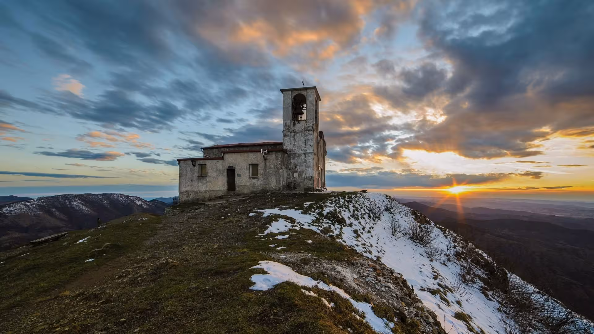 Historic church at sunset on Mount Tobbio, Capanne di Marcarolo Park, creating a dramatic and picturesque landscape.