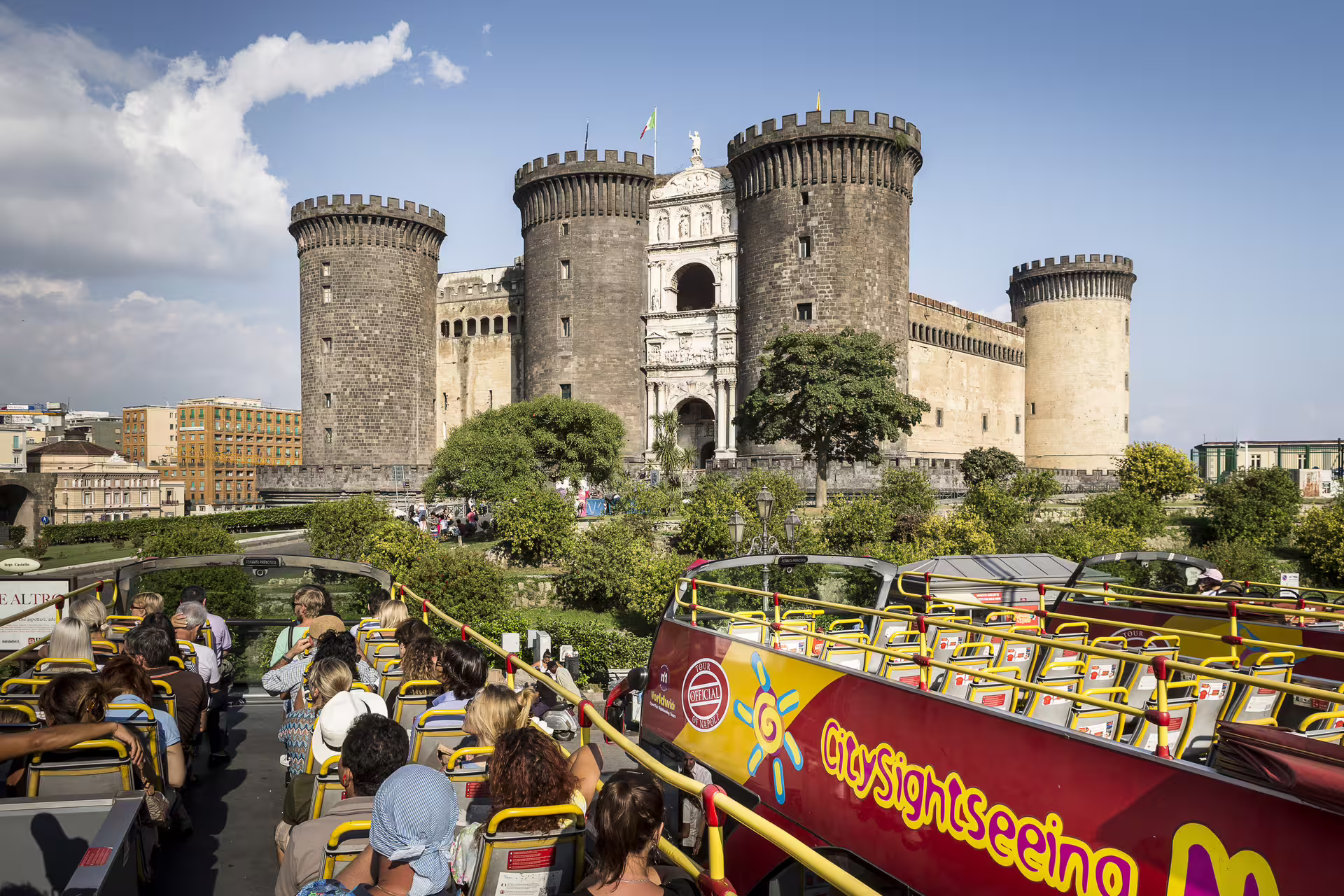 Tourists on open-top Naples hop on hop off bus admiring Castel Nuovo Maschio Angioino during panoramic city tour