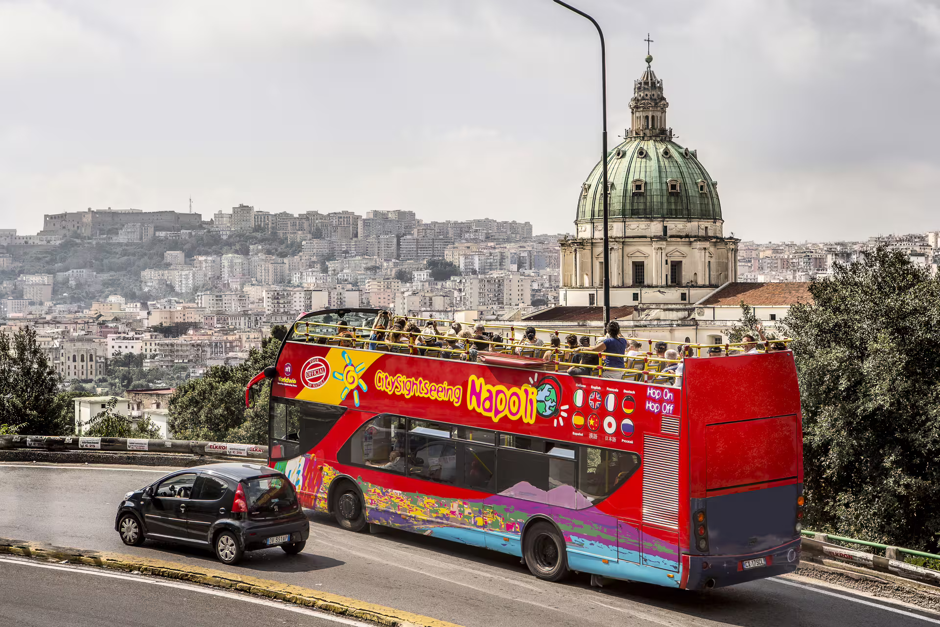 Open-top hop on hop off sightseeing bus in Naples passing a historic dome with panoramic views over the city skyline