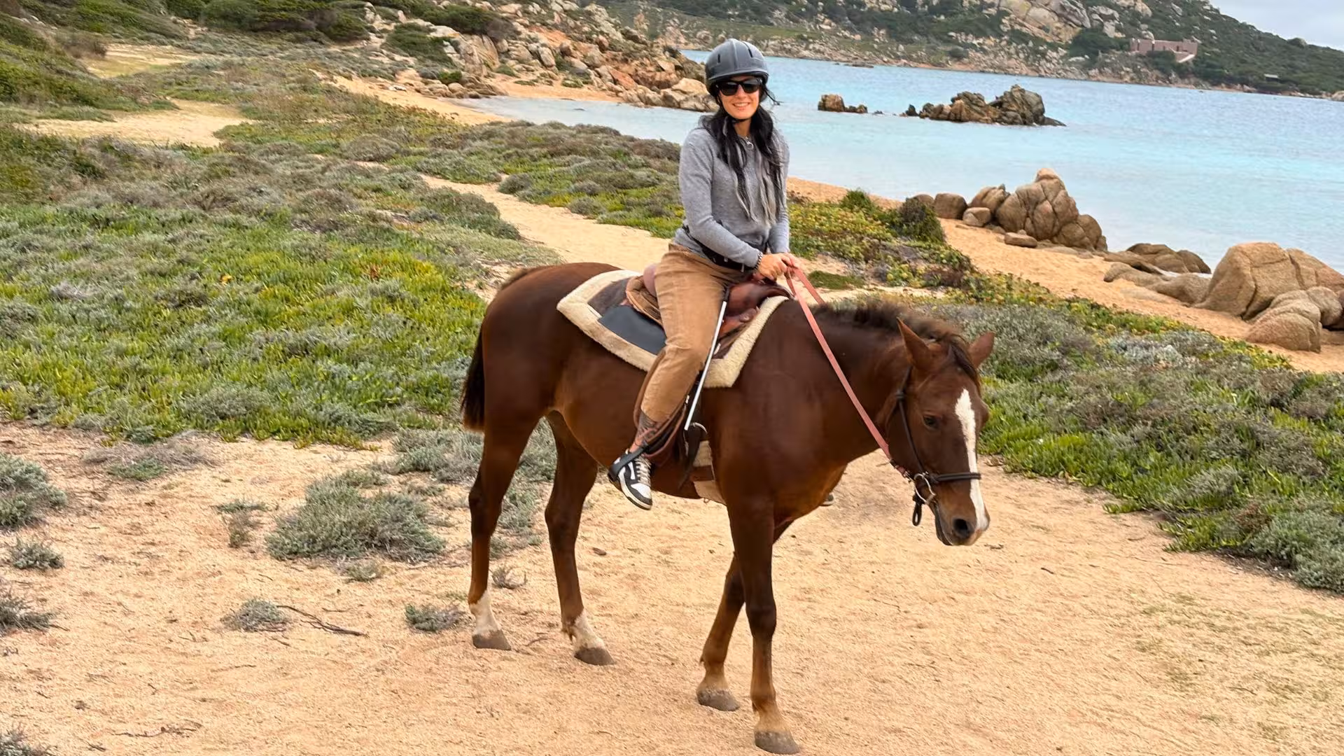 A rider on horseback explores the picturesque coastal trails of La Maddalena, surrounded by lush greenery.