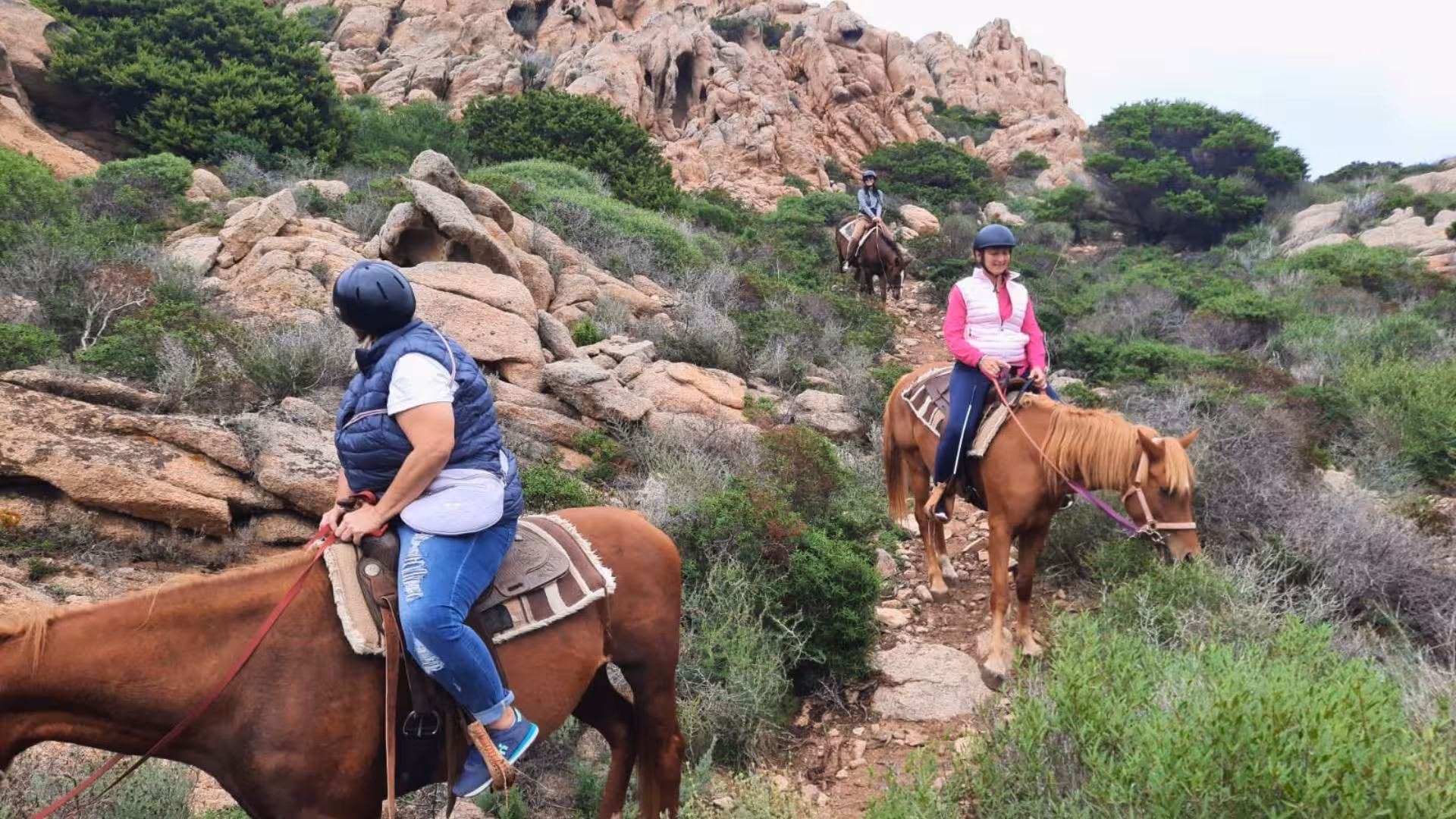 Participants on a horseback trail ride through rugged terrain in La Maddalena with stunning coastal views.