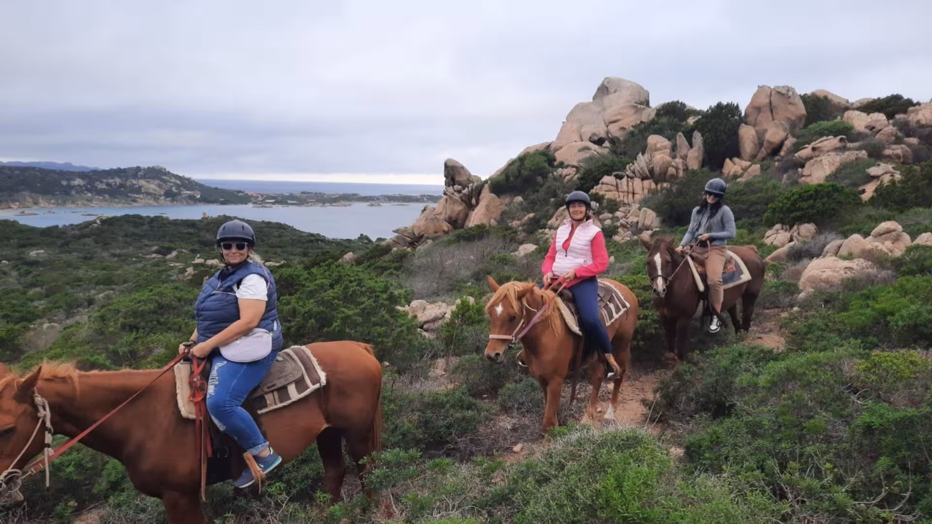 Three riders enjoying a scenic horseback tour on rocky hills overlooking the sea in La Maddalena, Palau.
