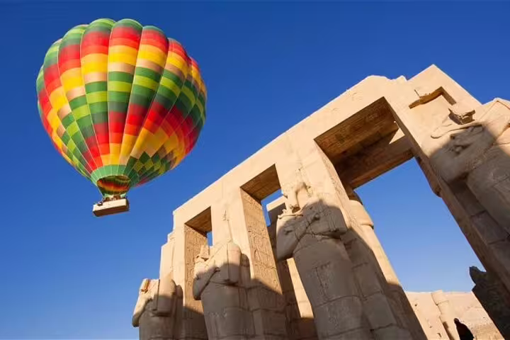 Colorful hot air balloon flying over Luxor Temple ruins, sunrise ride with hotel transfer in Luxor, Egypt