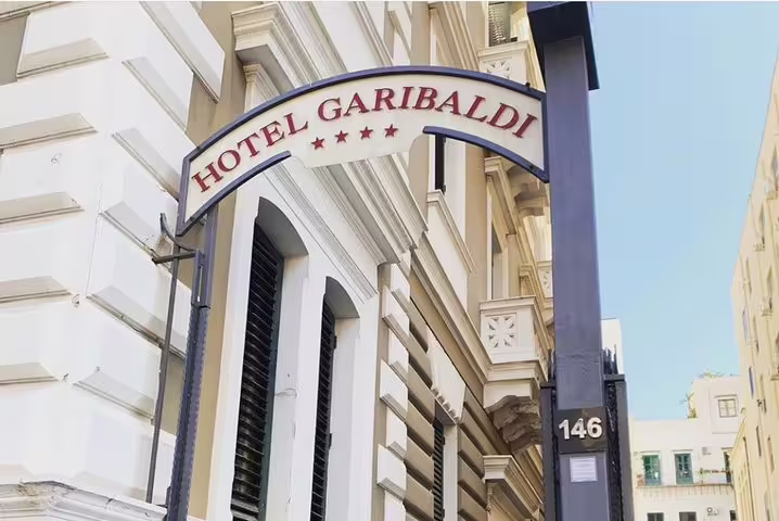 Street-level archway entrance of Hotel Garibaldi Palermo, showing four-star sign and city location for airport transfers