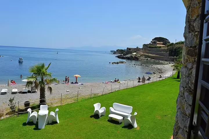 Sea-view lawn at Hotel Tonnara Trabia with modern white loungers facing the beach, ideal before a private transfer to Palermo Airport