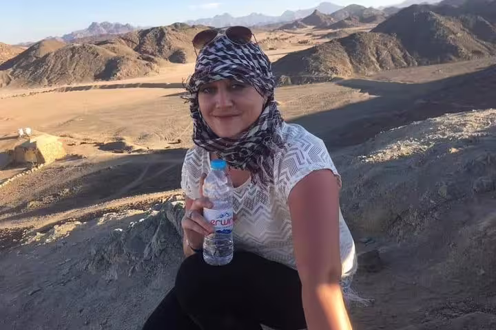 Guest in headscarf at desert viewpoint after quad bike safari, enjoying sunset scenery before Bedouin dinner