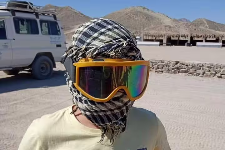 Desert safari guest wearing goggles and keffiyeh at quad bike base camp, ready for sunset ride and Bedouin dinner