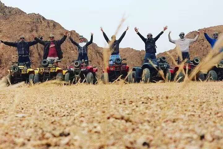 Group posing on quad bikes in the desert, perfect for a sunset desert safari with camel ride and Bedouin dinner