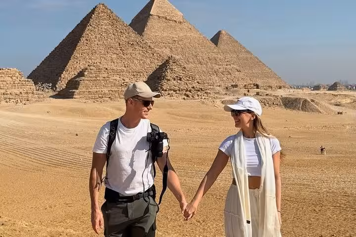 Couple holding hands in front of the Giza Pyramids on a Hurghada small group Cairo tour with Grand Egyptian Museum visit