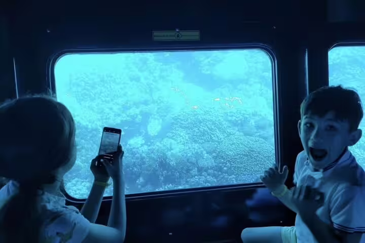 Kids viewing Red Sea coral reef from Hurghada panorama semi-submarine, taking photos on snorkeling sea excursion