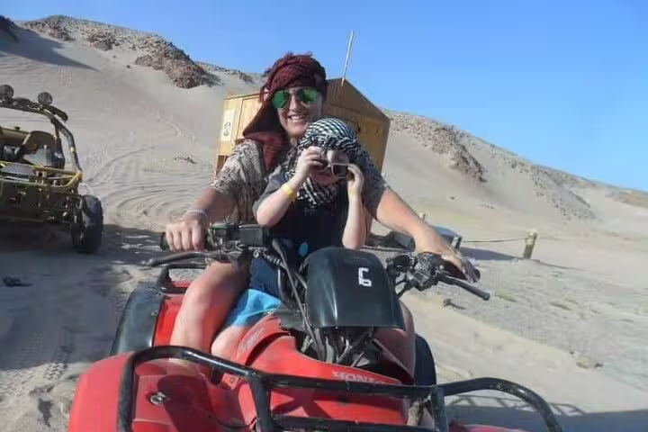 Family riding red quad bike on sand dunes, sunset desert safari with quad biking, camel ride and Bedouin dinner