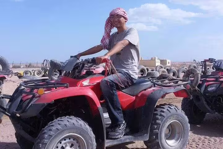Rider on red quad bike at desert camp, part of sunset desert safari with camel ride and Bedouin dinner