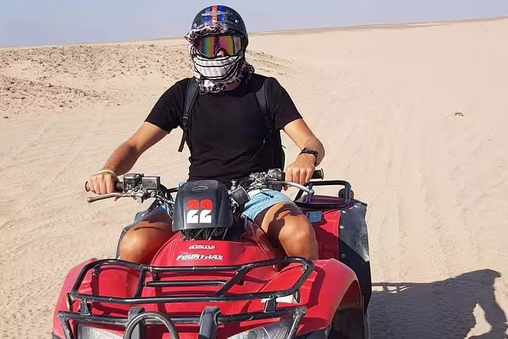 Rider on red quad bike crossing sandy dunes on a sunset desert safari adventure with Bedouin dinner