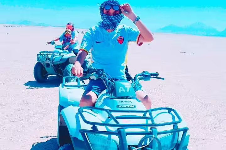 Two guests riding quad bikes across desert flats on a sunset safari tour with camel ride and Bedouin dinner