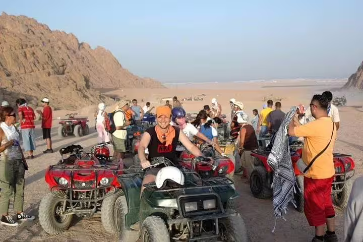 Group of riders on quad bikes in desert at sunset, gearing up for safari tour with camel ride and Bedouin dinner