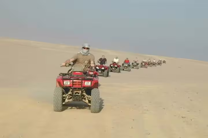 Quad bike convoy crossing golden dunes at sunset desert safari, adventure ride before camel trek and Bedouin dinner