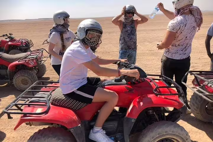 Riders wearing helmets on red quad bikes during a sunset desert safari adventure, before camel ride and Bedouin dinner