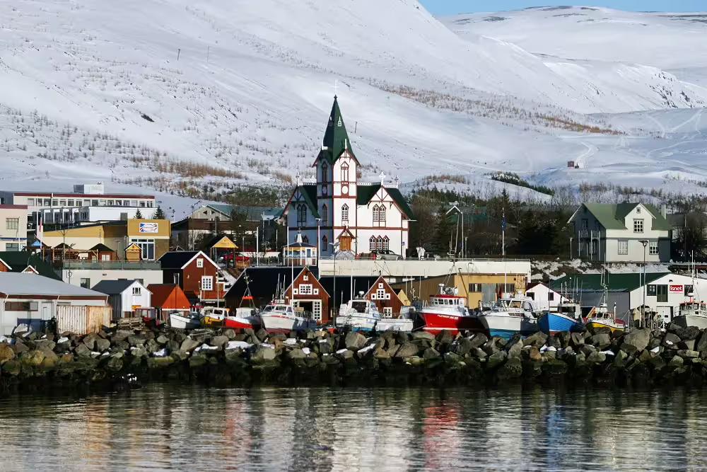 Husavik harbor with colorful boats, historic church, and snow-covered mountains in North Iceland