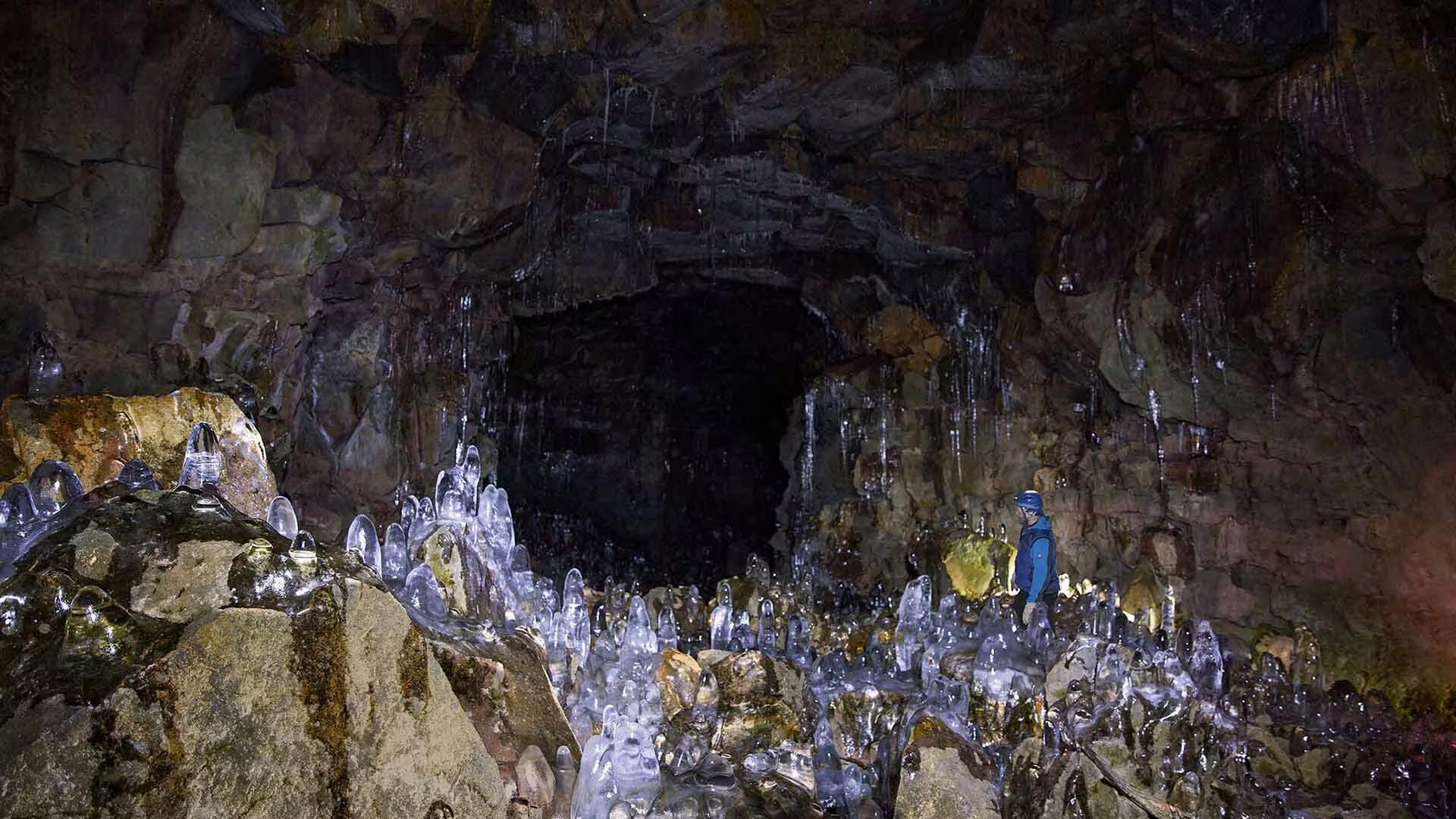 Explorer standing among ice stalagmites inside an illuminated Iceland lava tunnel cave