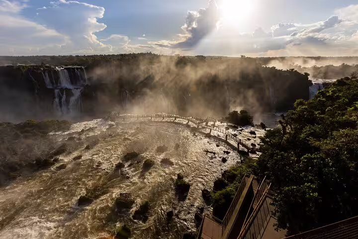 Aerial view of Iguazu Falls with mist rising and sun rays breaking through clouds on a guided tour adventure.