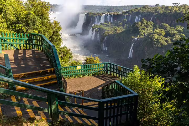 Stunning view of Iguaçu Falls from a vibrant green observation deck, showcasing cascading waterfalls and misty spray.