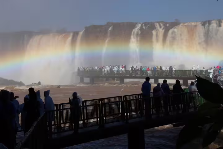 Tourists admire the majestic Iguazu Falls with a stunning rainbow arching over the powerful cascades in Brazil.