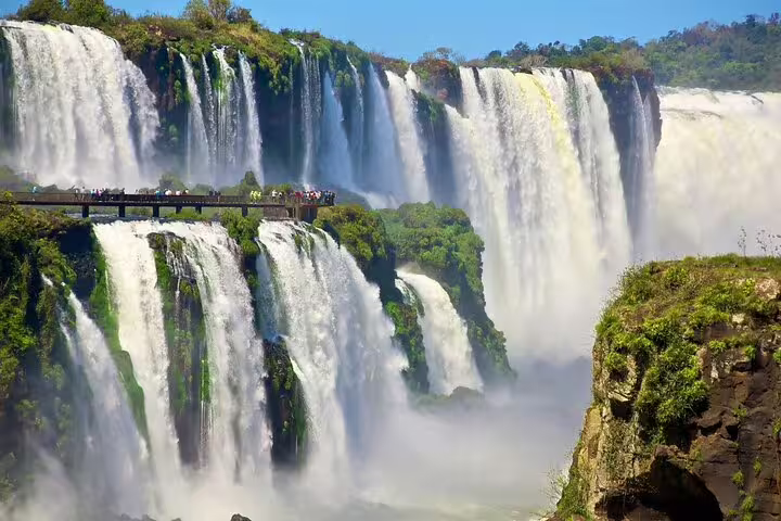 Tourists on a viewing platform admiring the stunning Iguazu Falls, surrounded by lush greenery and powerful cascades.