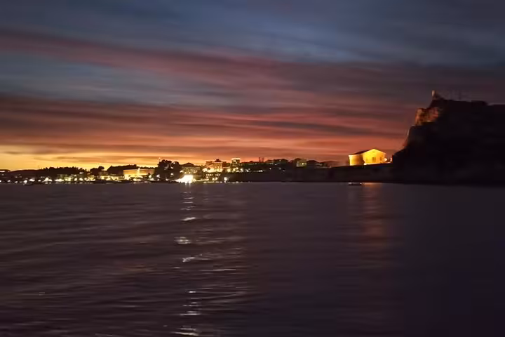 Ionian Sea sunset cruise with local BBQ boat trip, coastal village lights reflecting on calm water