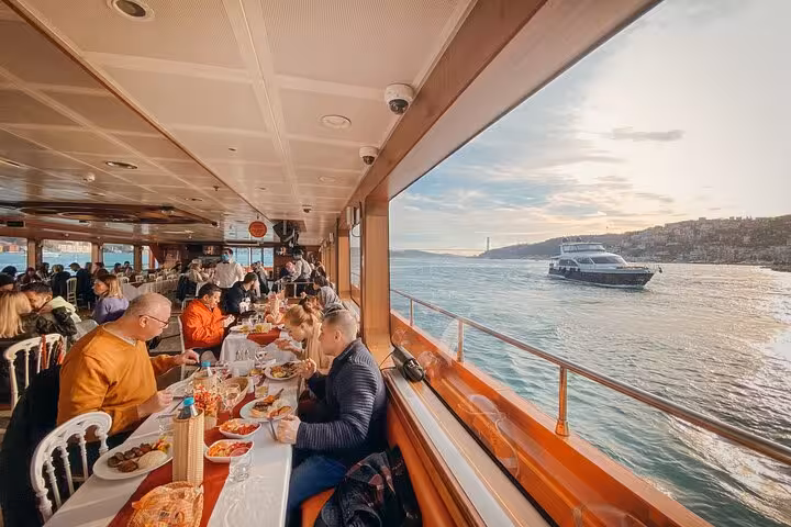 Guests enjoying Turkish dinner by panoramic windows on Istanbul Bosphorus cruise at sunset