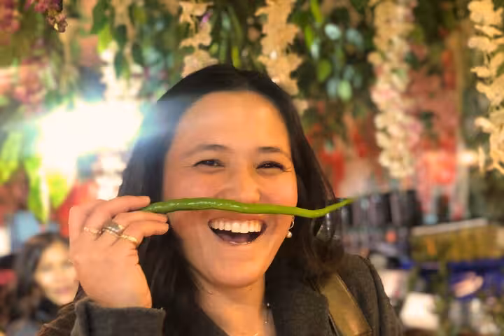 Smiling host at Istanbul city center market holds a green pepper, showcasing local flavors for cooking tour