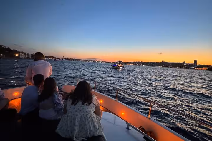 Guests relax on a luxury yacht at sunset, cruising the Bosphorus in Istanbul with city lights ahead
