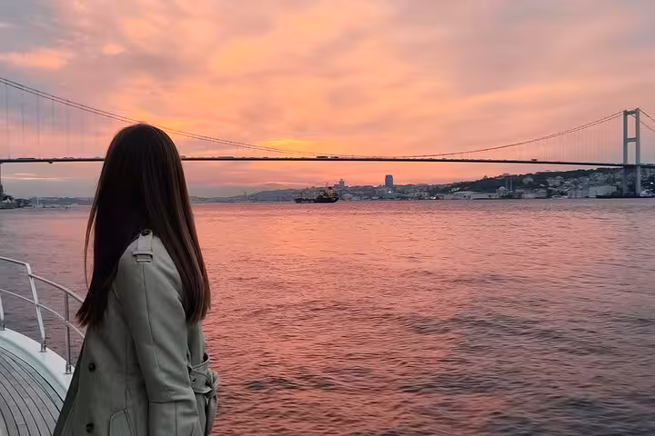 Guest on luxury yacht watching pink sunset over Istanbul Bosphorus with 15 July Martyrs Bridge