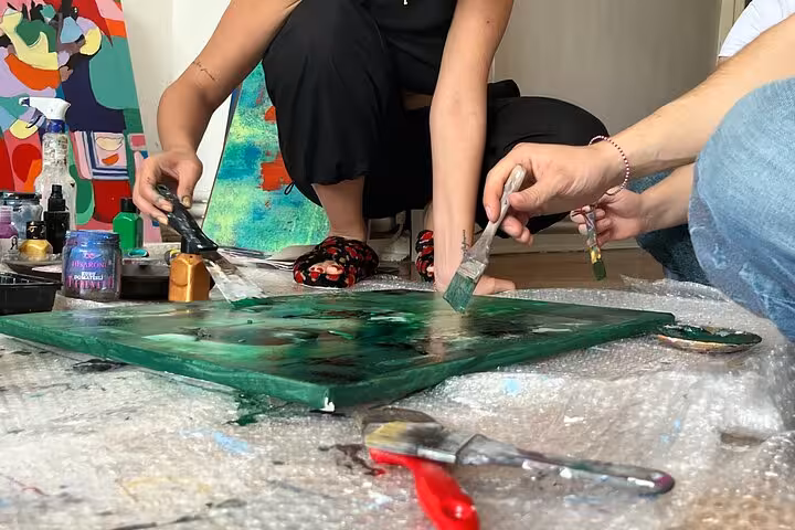 Guests paint abstract art with wine at a local home in Istanbul, hands brushing green canvas close-up